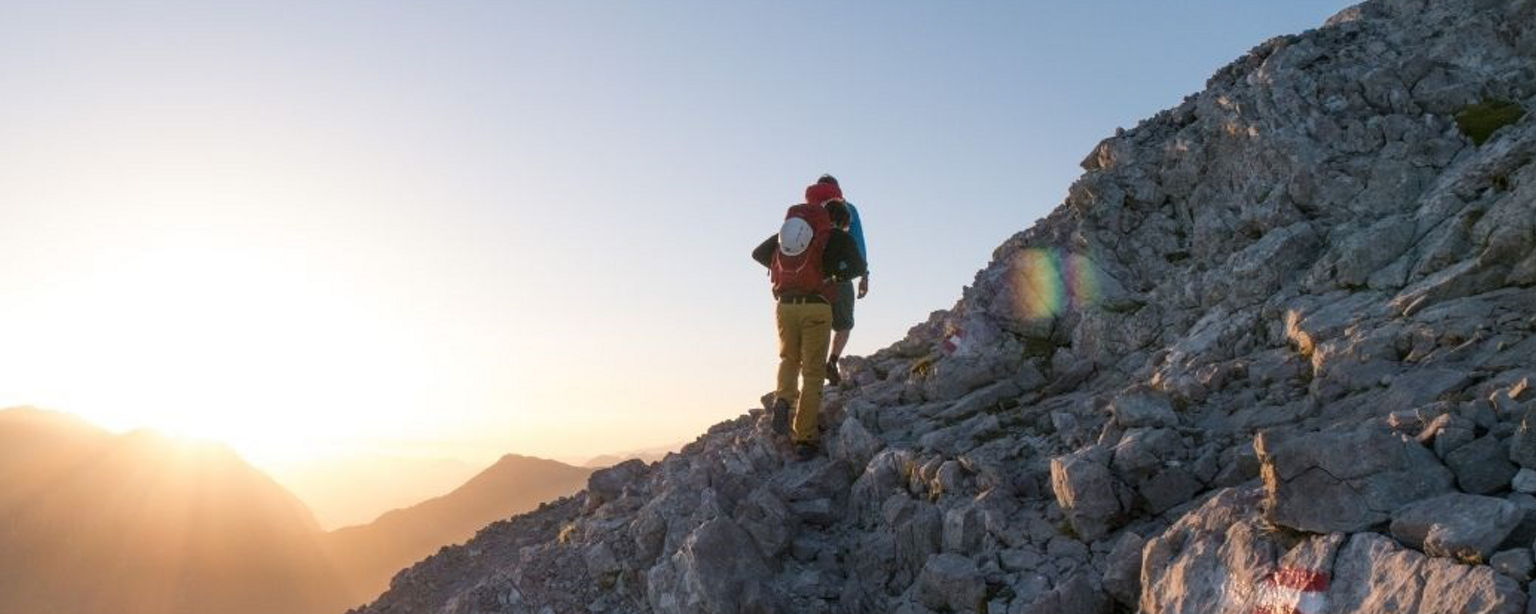 Zwei Bergsteiger bei Sonnenaufgang auf dem Weg zum Gipfel.